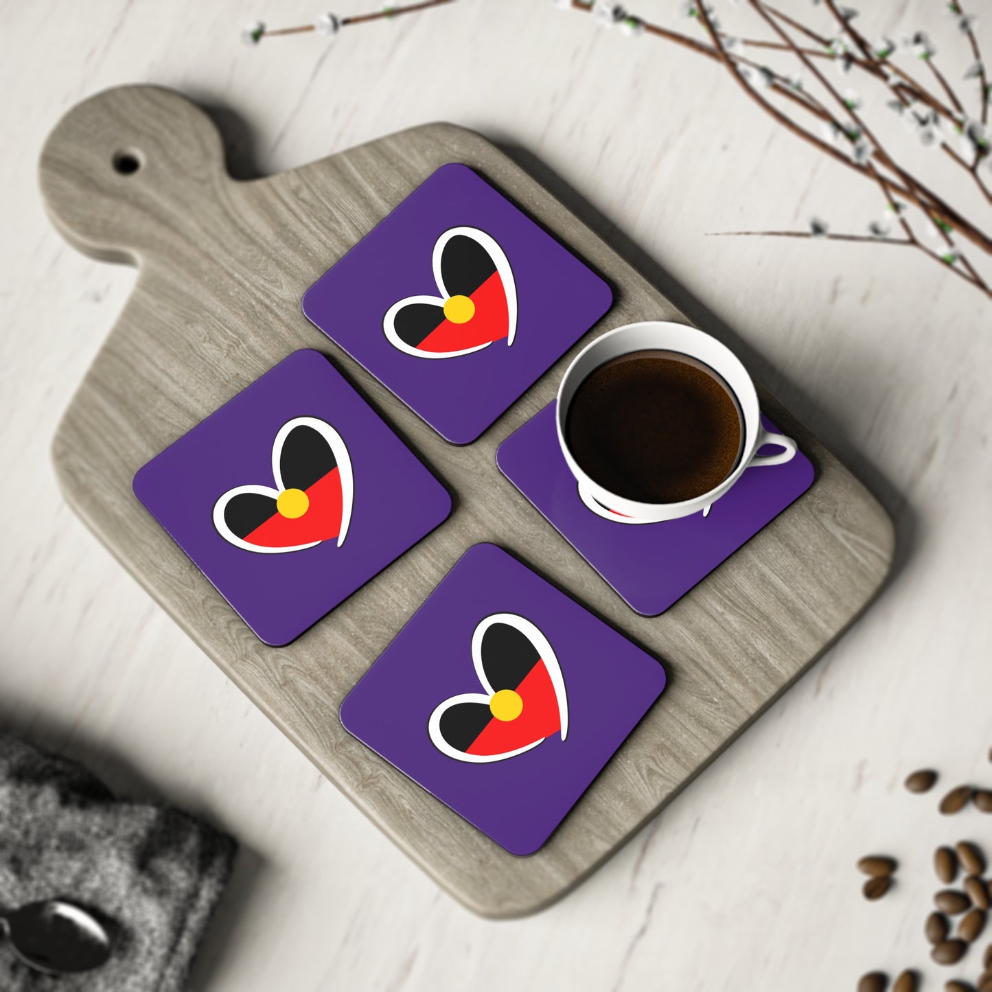 Four purple square coasters with Aboriginal heart design styled on timber board with coffee.