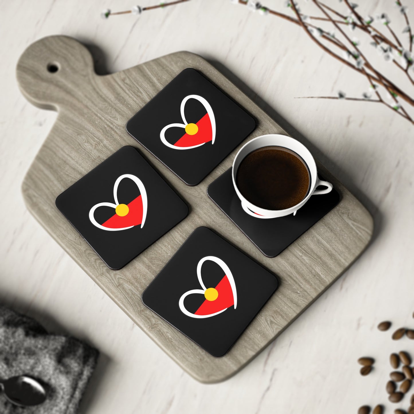 Set of four square black coasters displayed on serving board with cup and decorative setting.