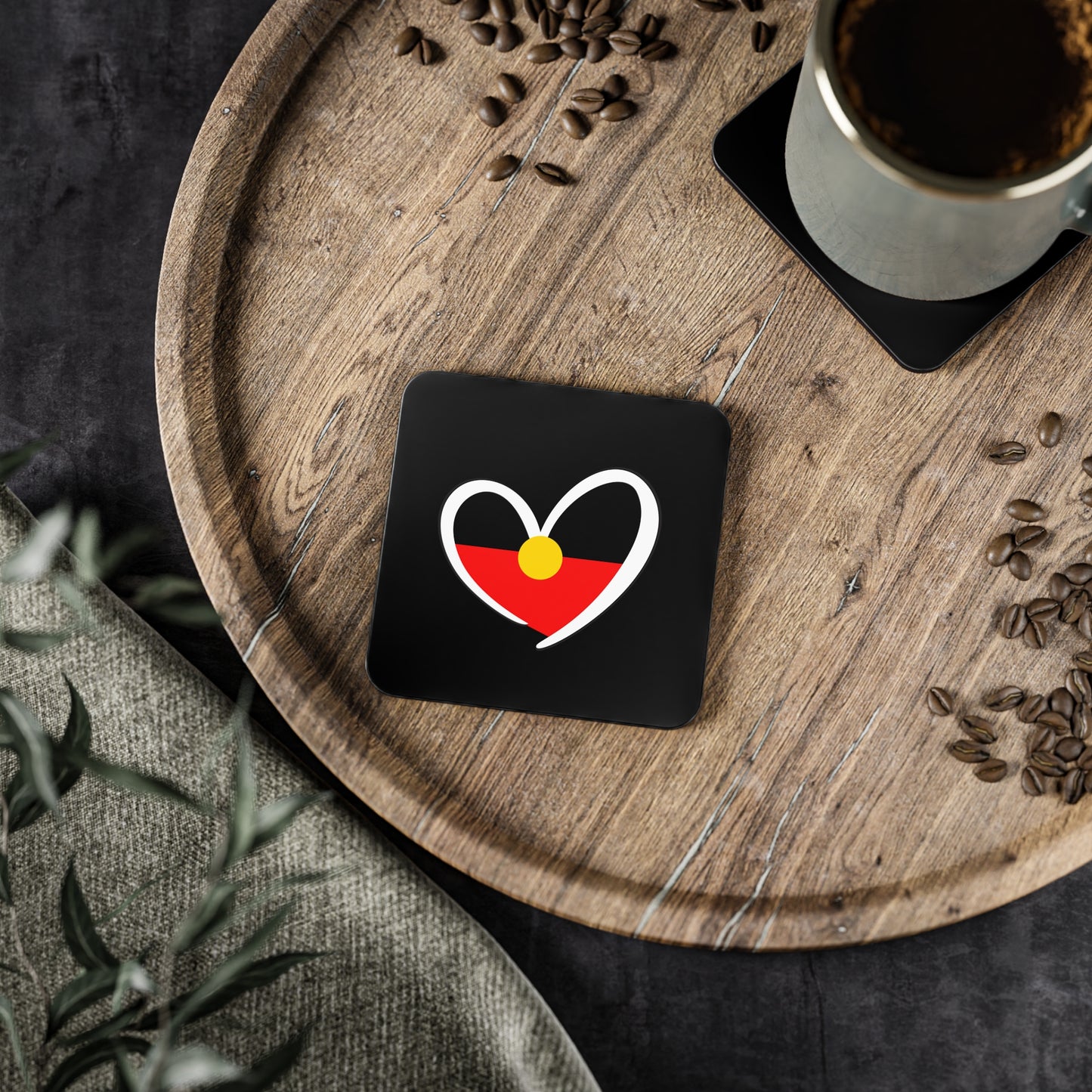 Square black Aboriginal Flag coaster on a wooden tray with coffee cup and coffee beans.