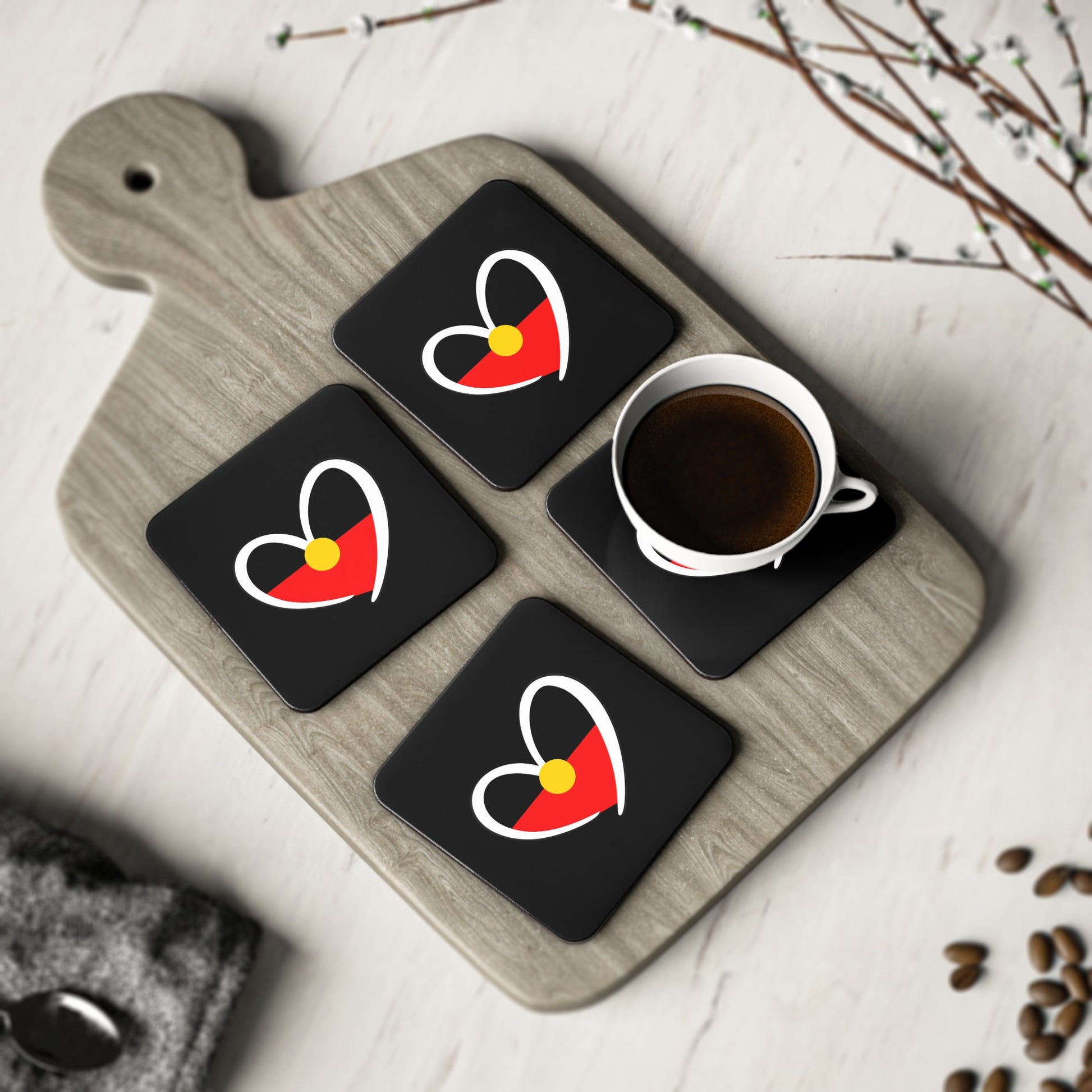 Set of four square black coasters displayed on serving board with cup and decorative setting.