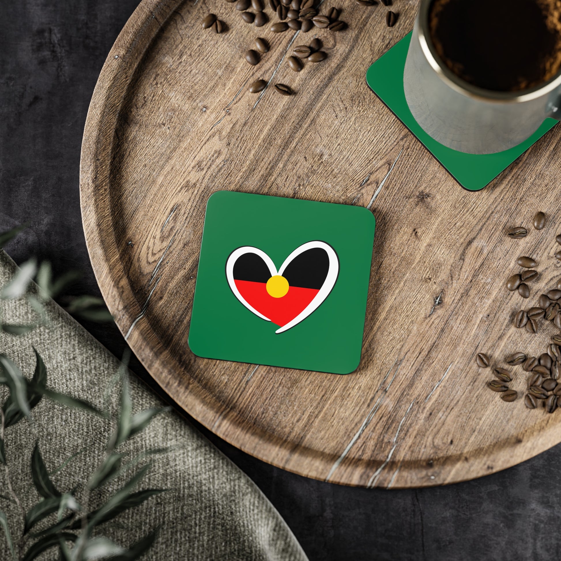 Stack of four square green coasters with Aboriginal heart design in red, black, and yellow.