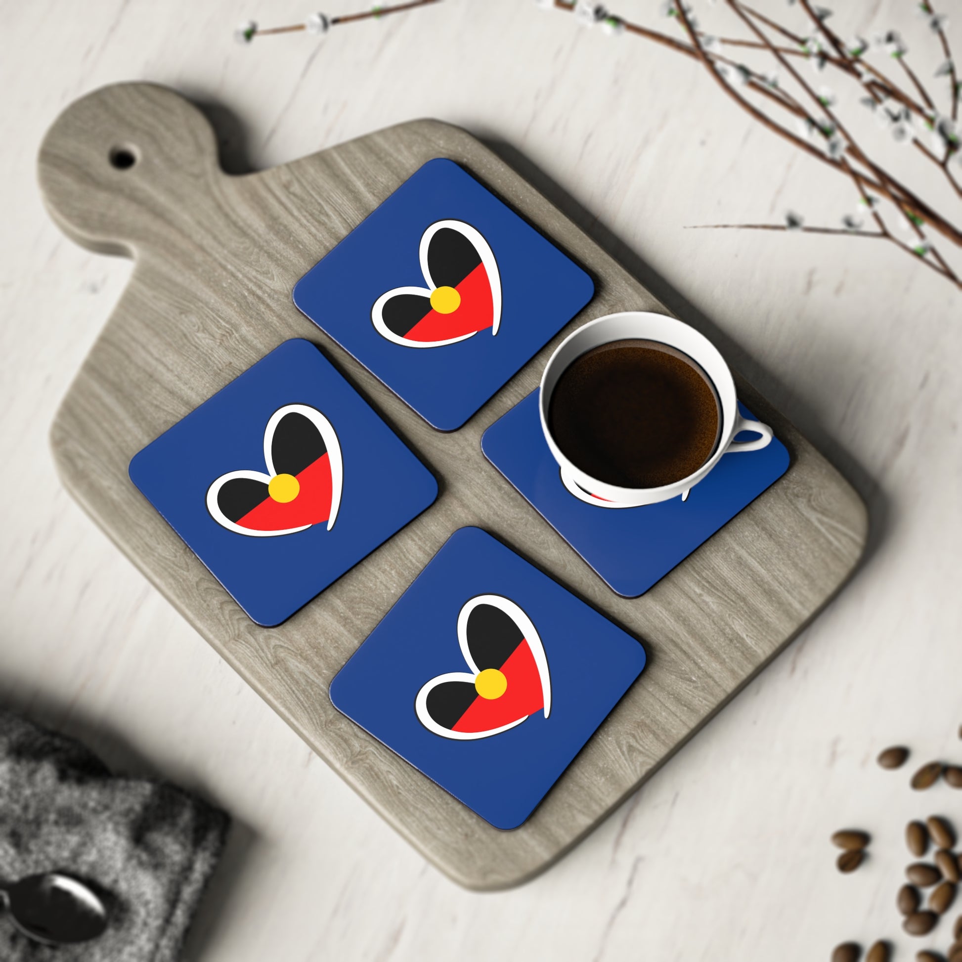 Set of 4 navy blue Aboriginal heart coasters styled with coffee cup on grey board – square shape.