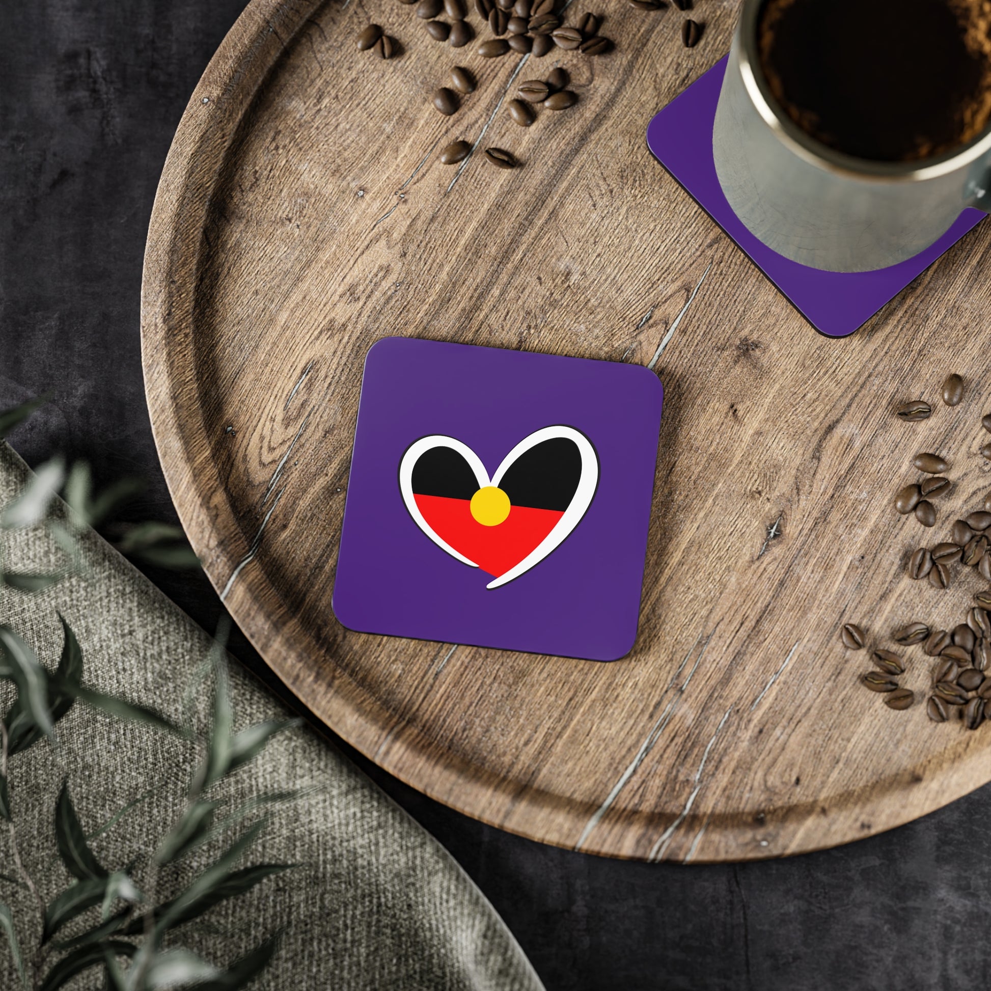 Square purple Aboriginal coaster with heart flag design shown in cosy home setting.